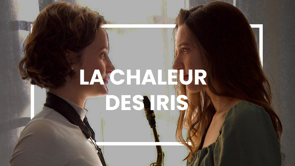 Deux jeunes femmes se font face, plongées dans un échange intense. L’une, aux cheveux courts et vêtue d’un haut blanc avec un harnais noir, tient un saxophone suspendu autour de son cou. L’autre, aux longs cheveux ondulés et portant une robe verte, semble captivée. La lumière douce filtrant à travers un rideau confère une atmosphère intime et chargée d’émotion. Le titre “LA CHALEUR DES IRIS” apparaît en blanc au centre, renforçant l’intensité du regard échangé.
