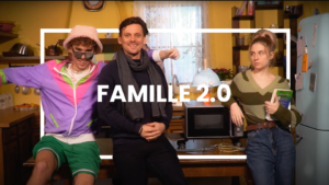 Trois personnages aux styles très différents sont réunis dans une cuisine à l’ambiance rétro et chaleureuse. À gauche, un jeune homme excentrique, vêtu d’un survêtement coloré des années 90, d’un bob rose et de lunettes de soleil, adopte une pose décontractée et expressive. Au centre, un homme en écharpe et veste sombre affiche un sourire serein, contrastant avec l’énergie débordante de son voisin. À droite, une jeune femme en pull rayé vert, un livre à la main, semble sceptique face à la scène. Le titre “FAMILLE 2.0” inscrit en blanc au centre illustre une dynamique familiale moderne et haute en couleur.
