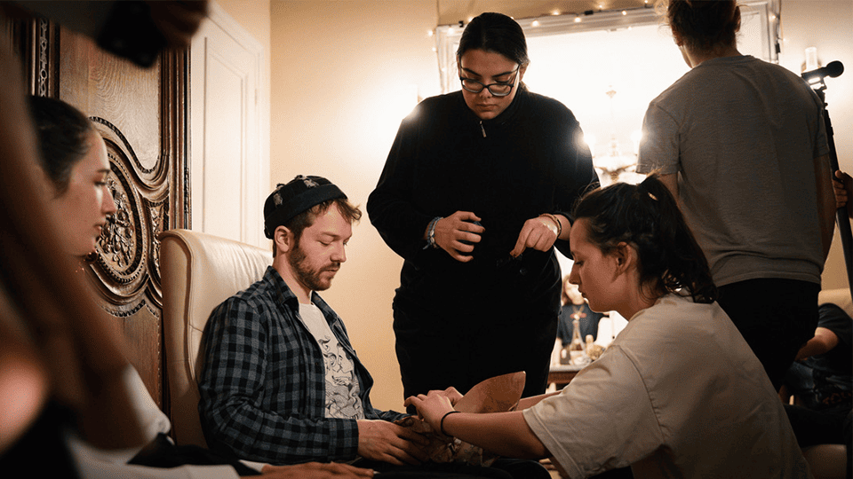 Équipe de tournage en pleine préparation sur le plateau d’un court-métrage, concentrée autour d’un acteur assis pendant les réglages de maquillage et de costume.