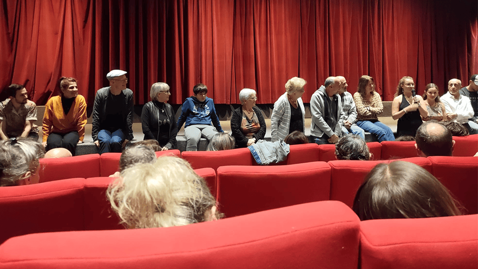 Équipe d’un film assise devant un rideau rouge lors d’un échange avec le public dans une salle de cinéma, face à des spectateurs installés dans des fauteuils rouges.