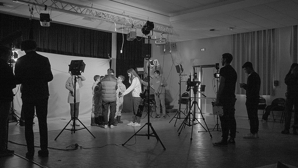 Tournage en studio d’un court-métrage scolaire avec une équipe technique en pleine préparation, entourée de projecteurs et d’équipements audiovisuels.