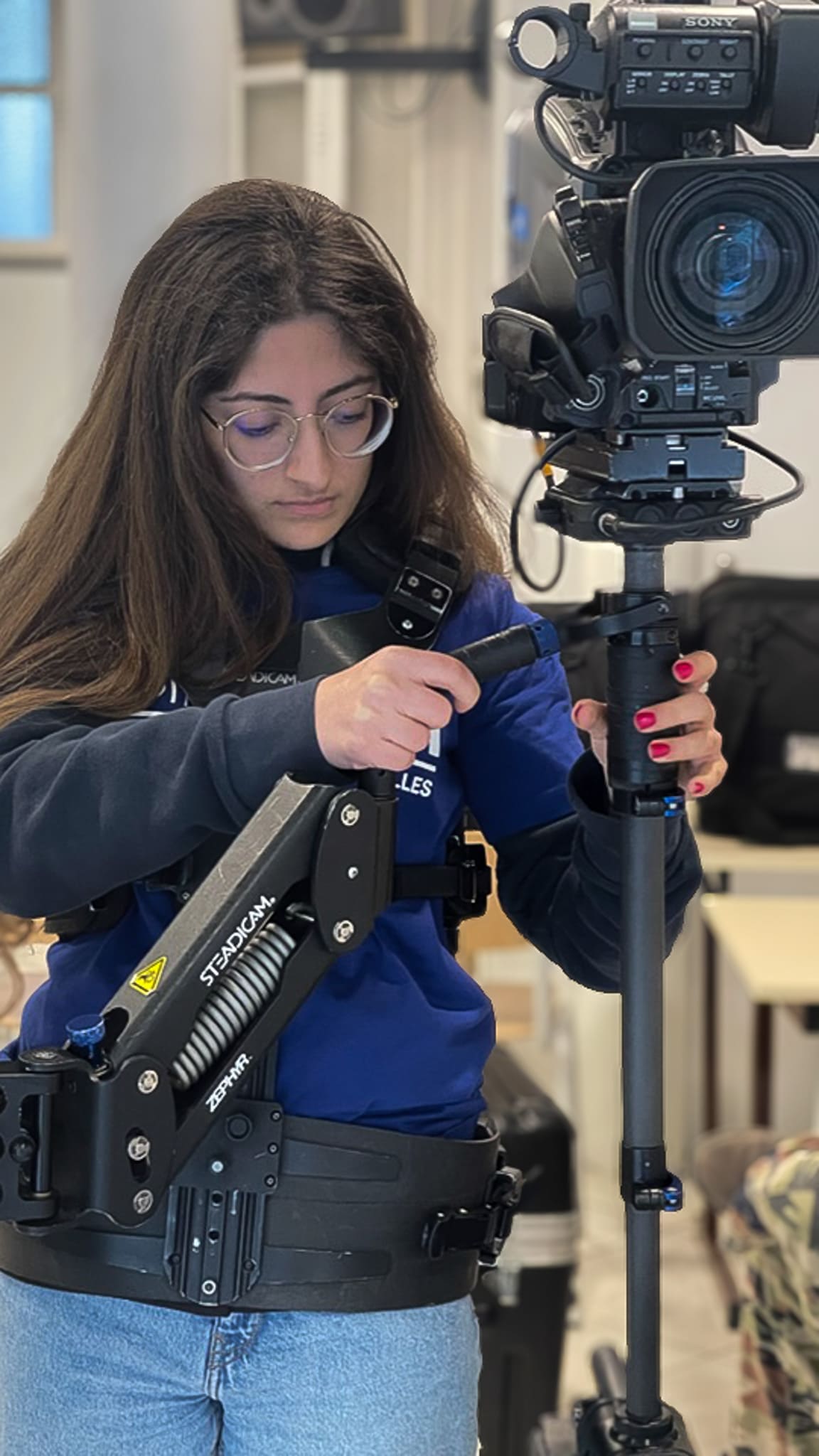 Étudiante en audiovisuel manipulant un steadicam professionnel. Elle ajuste l’équipement pour stabiliser une caméra Sony, concentrée sur son travail en environnement studio.