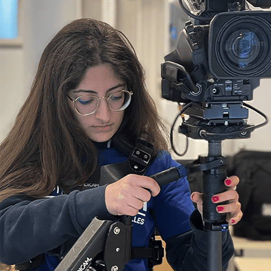 Étudiante en audiovisuel manipulant un steadicam professionnel. Elle ajuste l’équipement pour stabiliser une caméra Sony, concentrée sur son travail en environnement studio.
